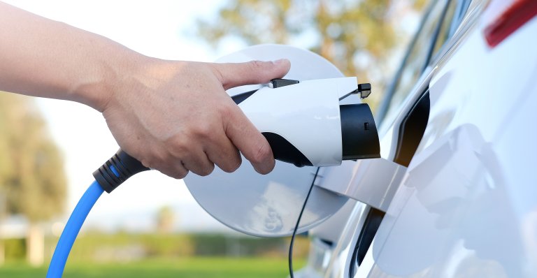 Electric car or ev is charging at station . man use the white power cable and plug on nature background. eco and clean energy concept with the mobile phone smart technology. zero gas no transmission.jpeg